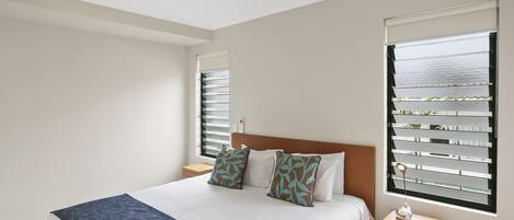 A bedroom with a bed, nightstands, a lamp, and a window with blinds.