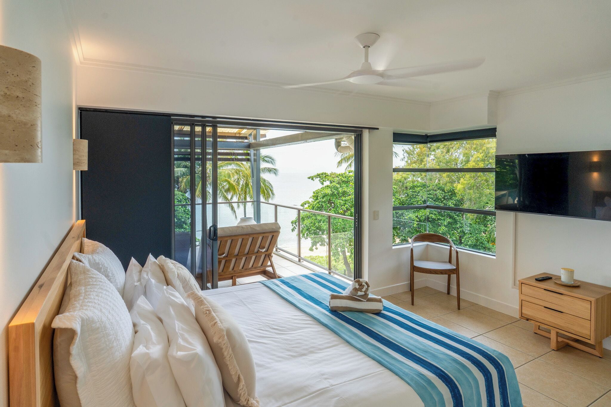 A bedroom with a bed, a chair, a TV, and a balcony with a view of trees.