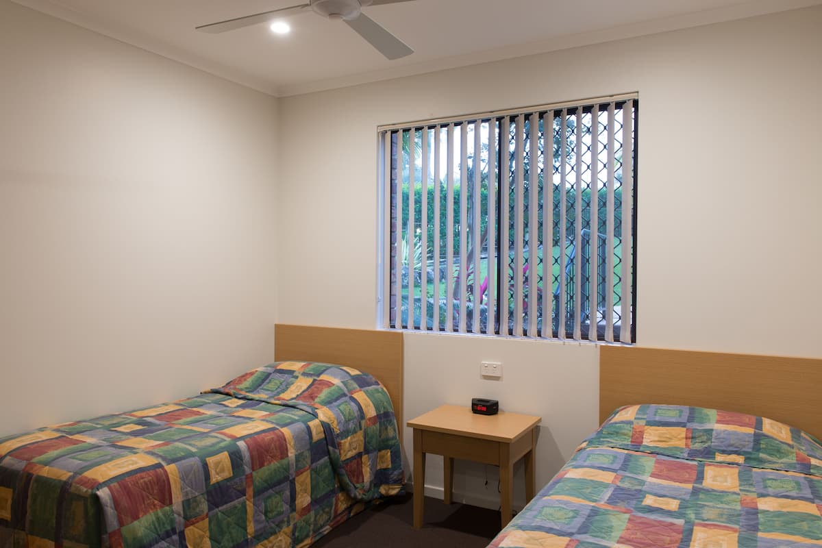 A bedroom with two beds, a small table, and a window with blinds.