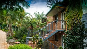 Una casa con fachada de ladrillo, escalera de metal y exuberante vegetación tropical.