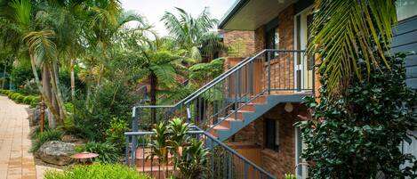 A house with a brick exterior, a metal staircase, and lush tropical vegetation.