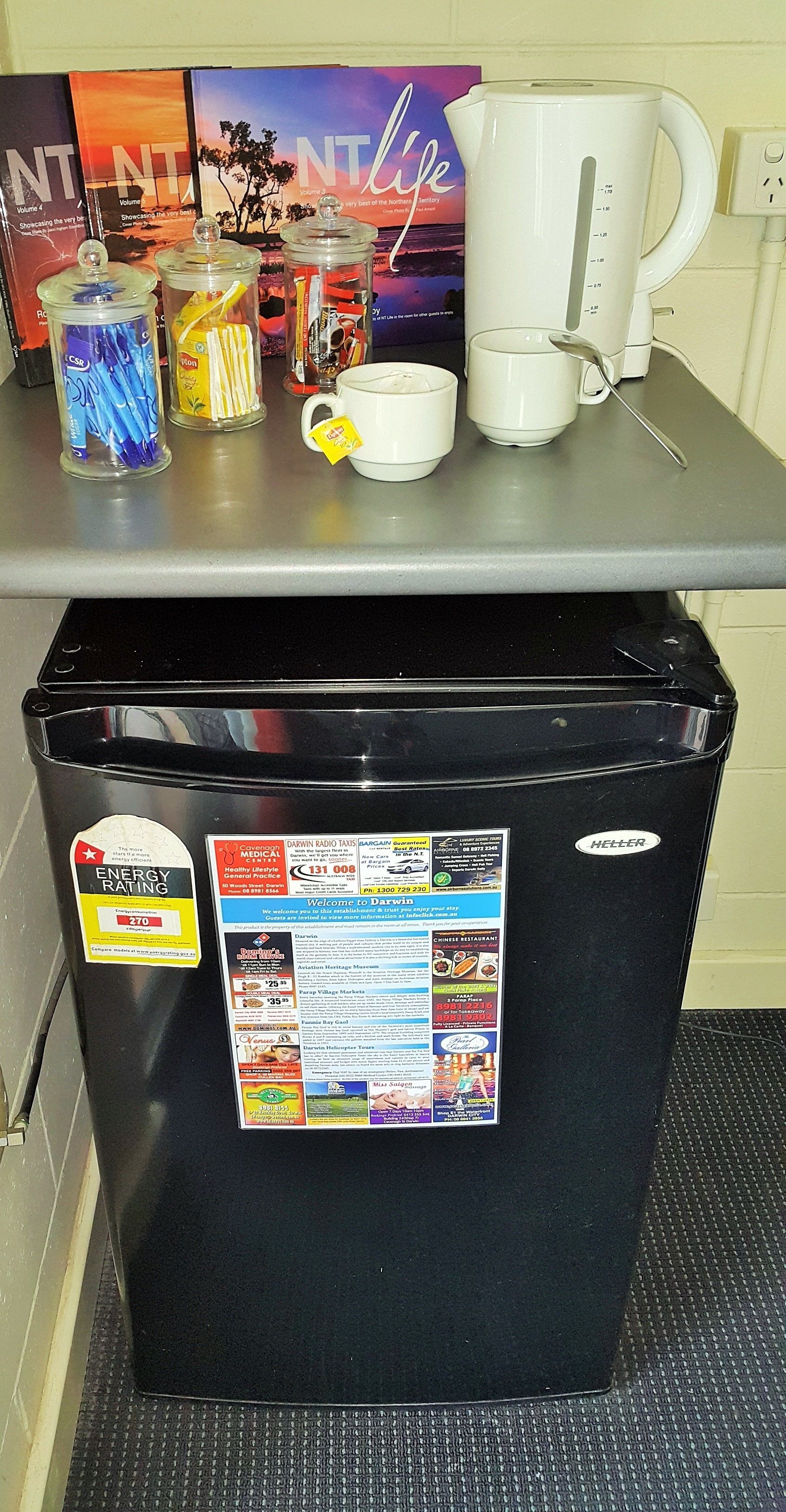 Een aanrecht met een koffiezetapparaat, een mok en een prullenbak met verschillende stickers.