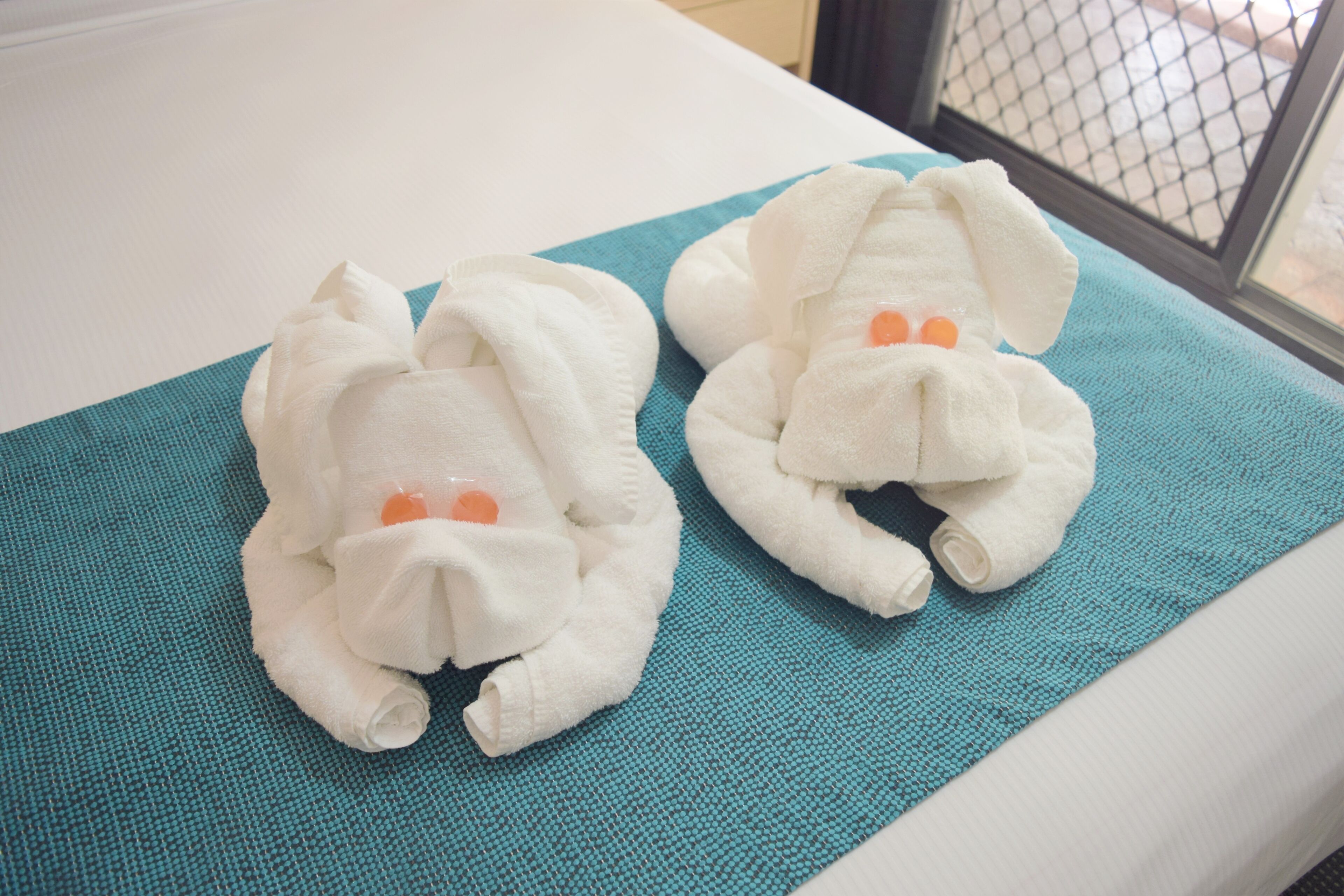 Two towels shaped like white rabbits on a teal towel on a bed.