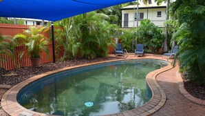 A swimming pool with a brick border, surrounded by palm trees and a blue canopy. - Coconut Grove Holiday Apartments (Coconut Grove)