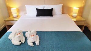 A hotel room with a large bed, two nightstands, two lamps, and two plush toys on the bed. - Coconut Grove Holiday Apartments (Coconut Grove)