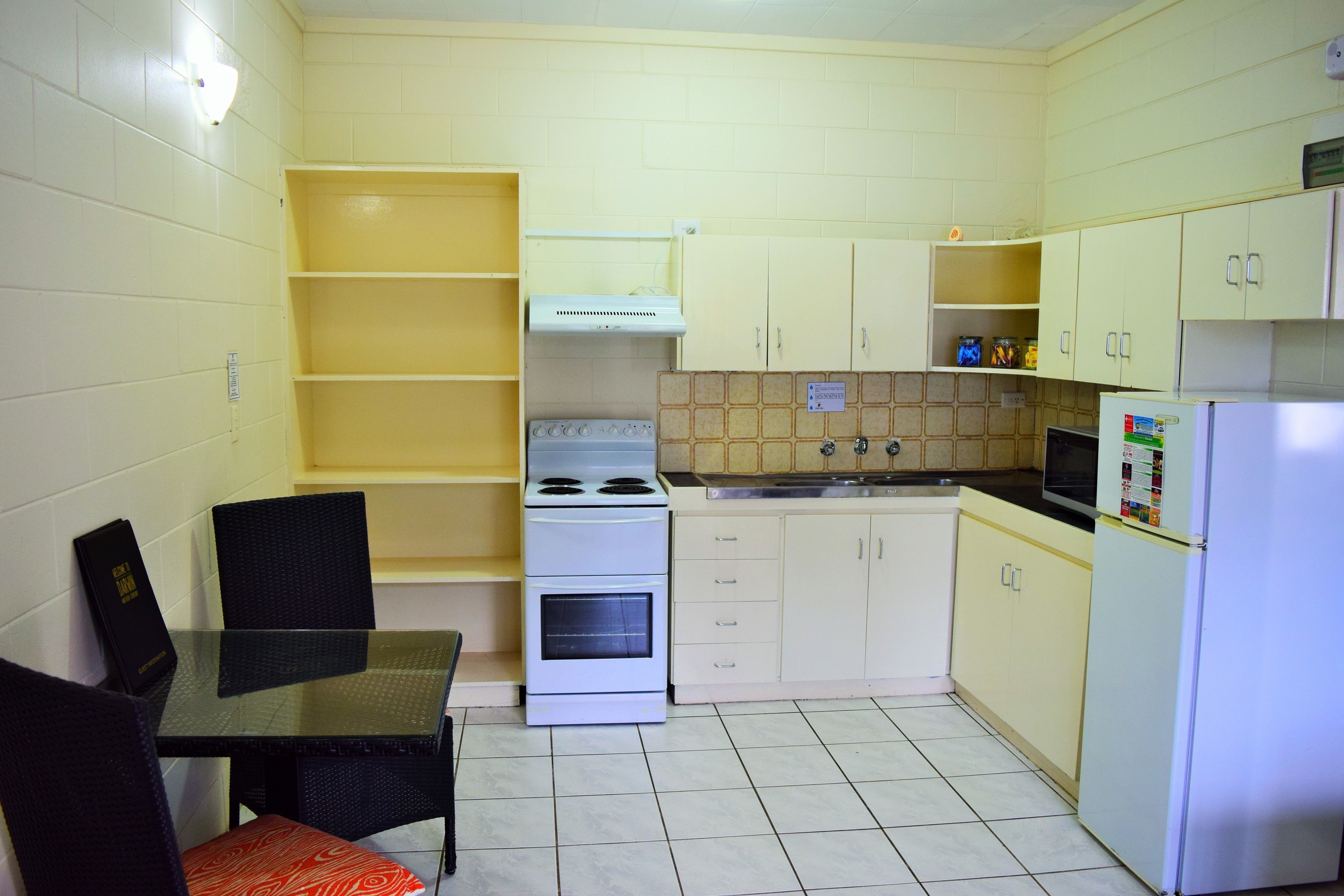 Una cocina compacta con gabinetes blancos, estufa, refrigerador y una mesa de comedor con sillas.