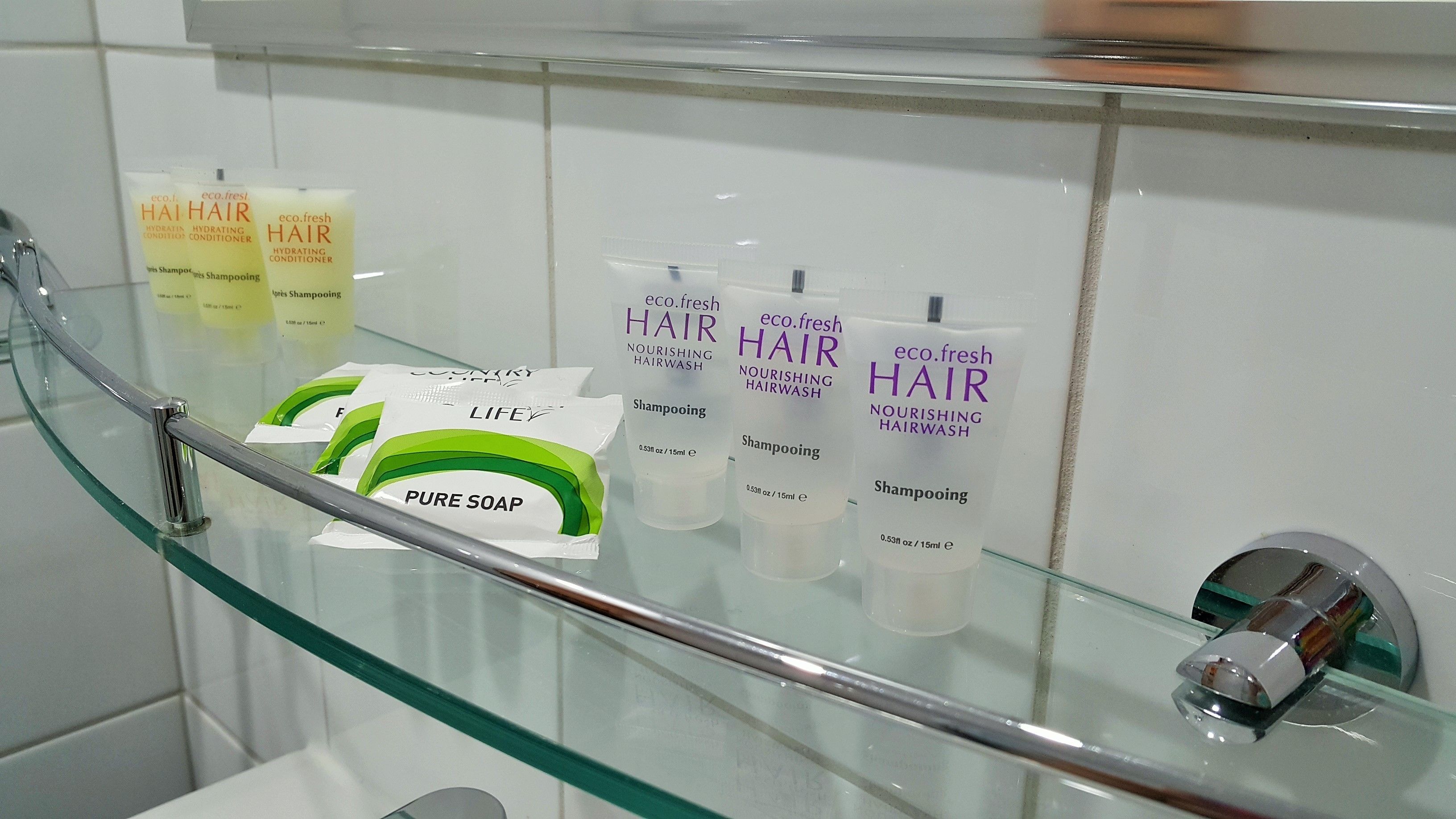 A bathroom with a glass shelf displaying various hair care products.