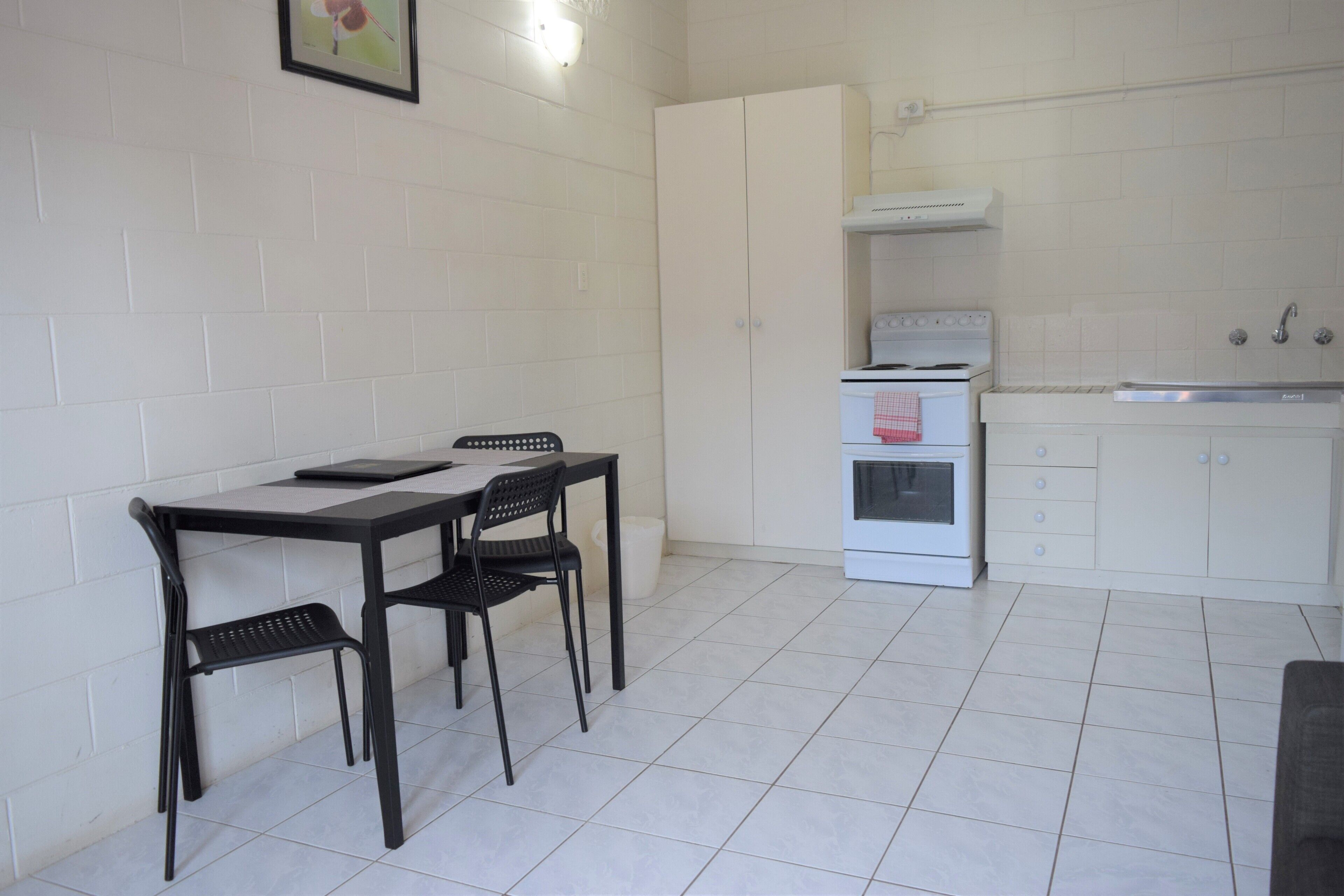 A compact kitchen with white cabinets, a white stove, and a small countertop. There is a dining table with two chairs.