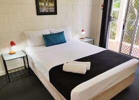 Una habitación de hotel con una cama grande, ropa de cama blanca, una almohada azul, dos mesitas de noche con lámparas y una ventana con vistas a zonas verdes.