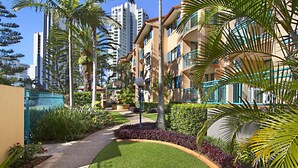 A residential area with a pathway, palm trees, and modern buildings with balconies. - Aruba Surf Resort (Broadbeach)