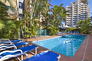 A pool area with lounge chairs, palm trees, and a tall building in the background.