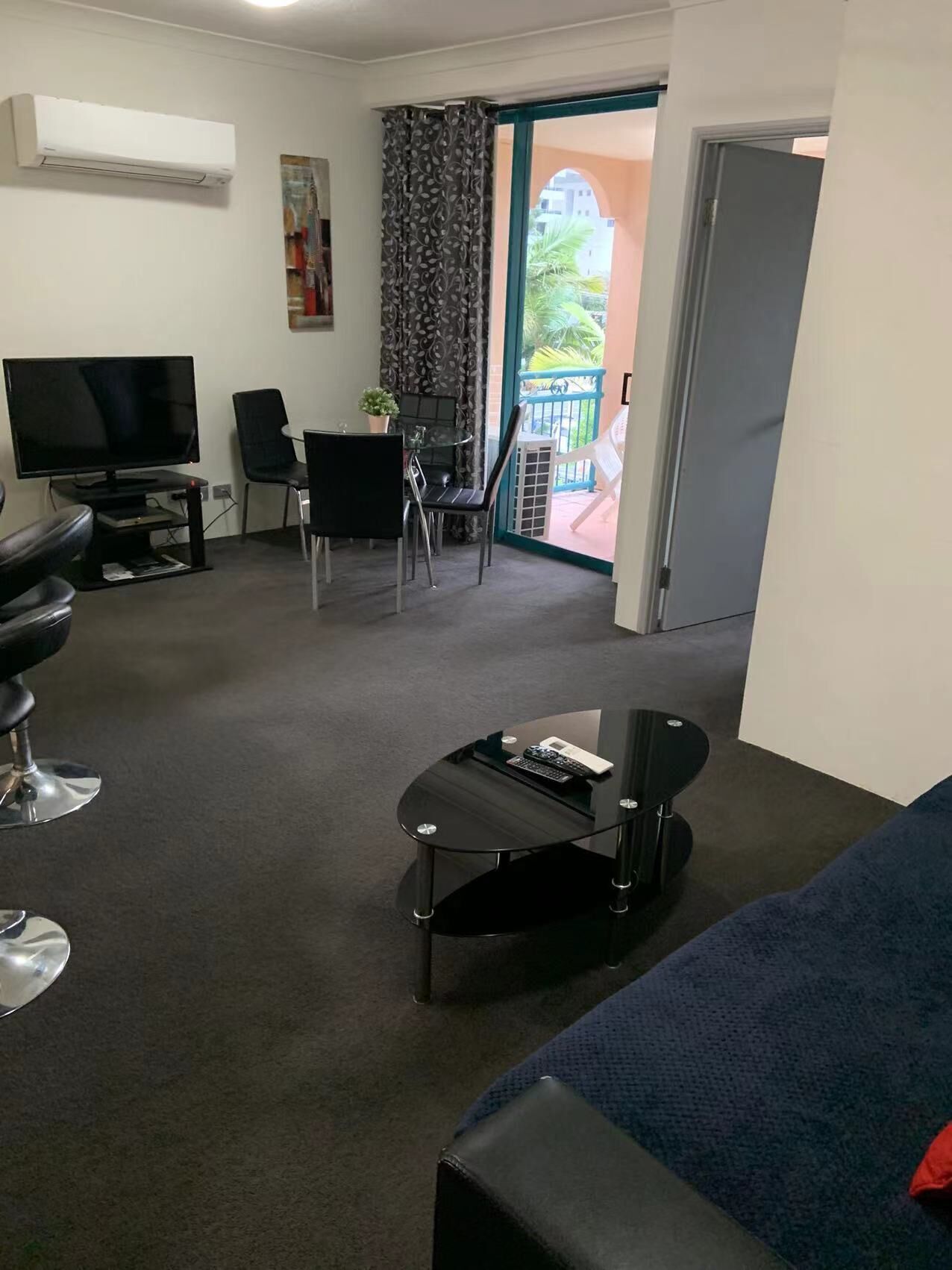 Hotelkamer met een televisie, een zithoek met stoelen, een kleine tafel met afstandsbediening, een bank en een balkon met uitzicht.