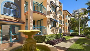 A courtyard with a fountain, a pool, and a building with balconies and windows. - Aruba Surf Resort (Broadbeach)