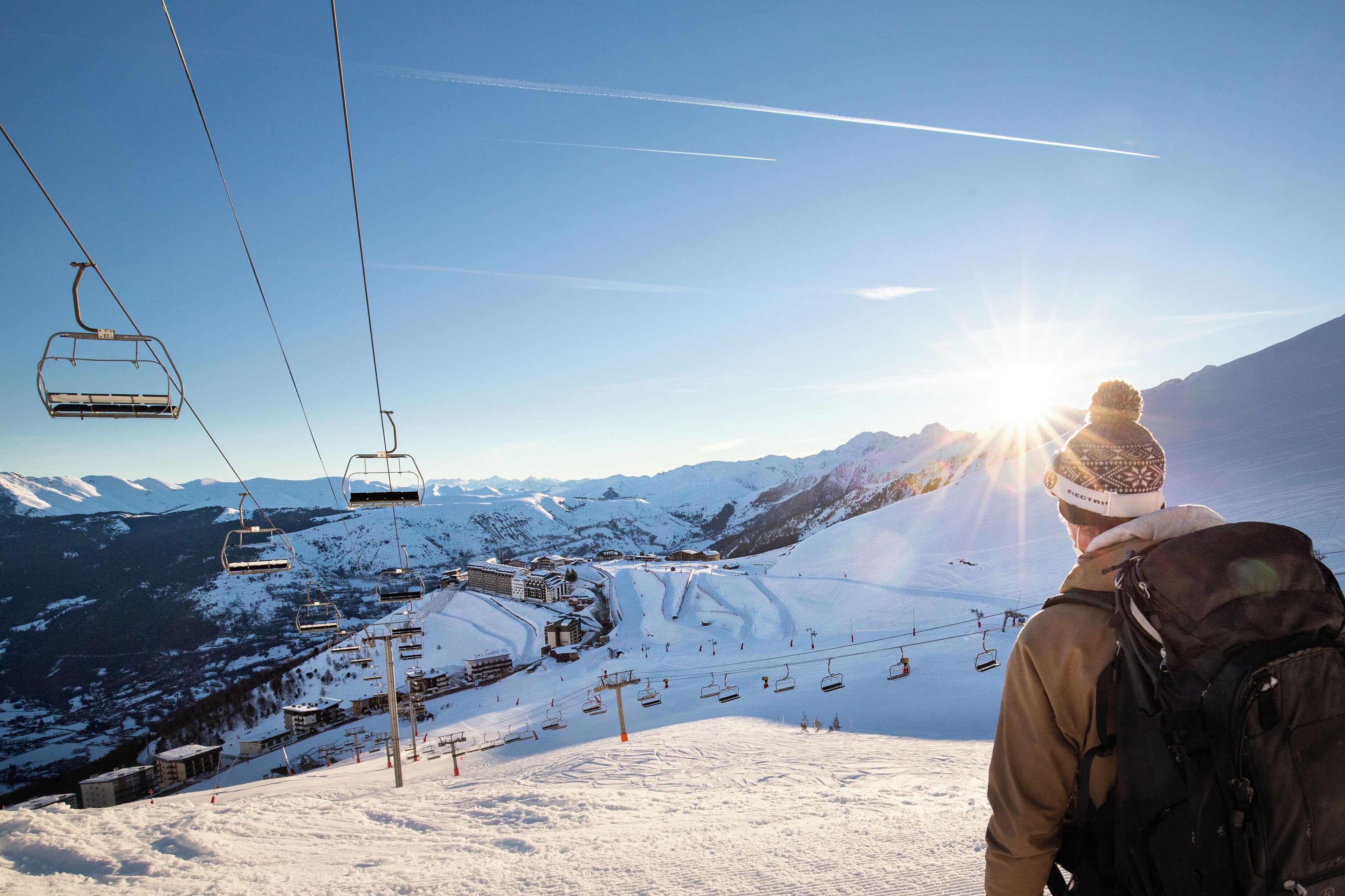 A ski lift with cabins, a snowy mountain landscape, and a clear sky.