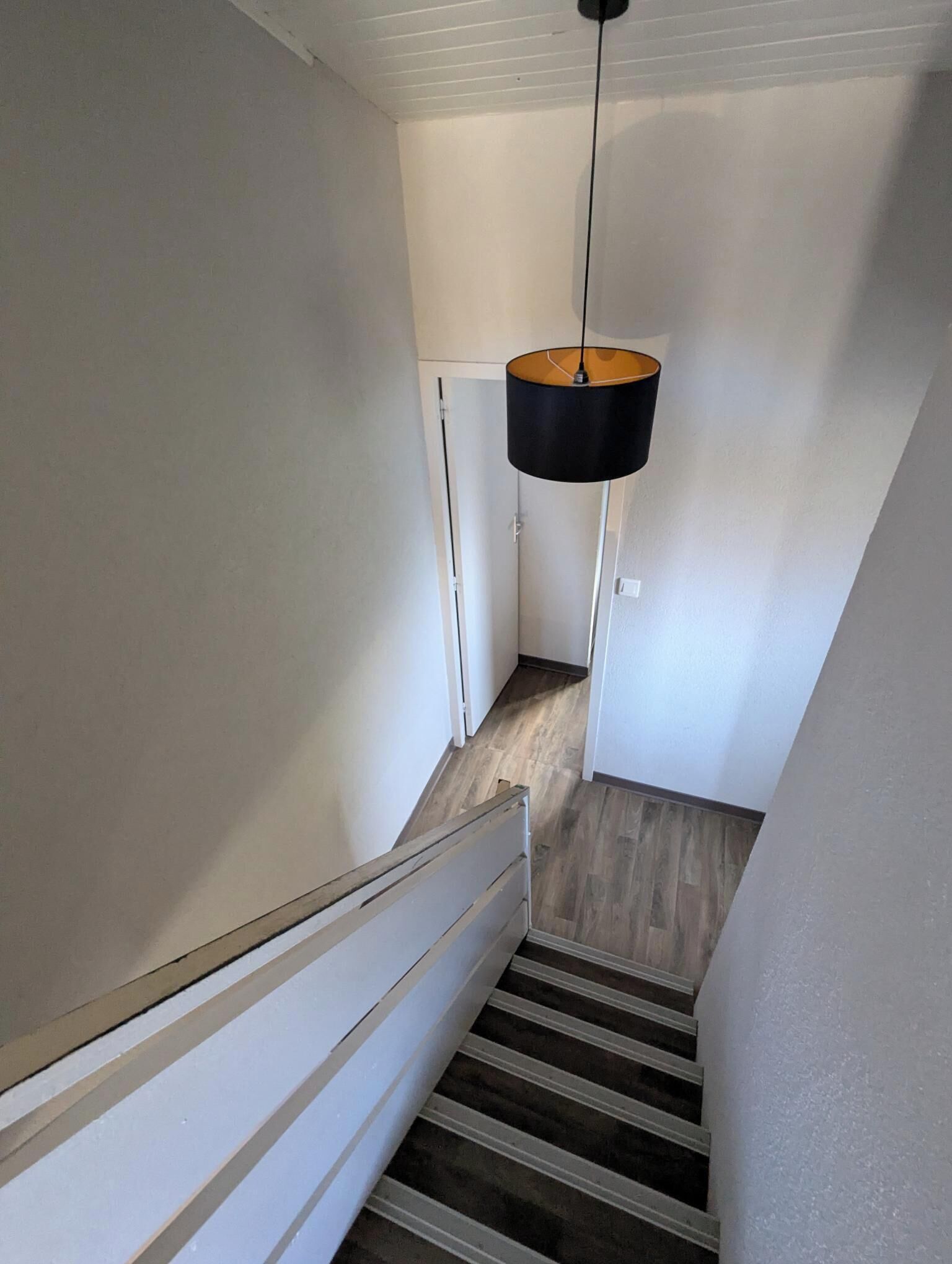 Eine enge Treppe mit Holzsitzen und einem weißen Geländer, die zu einer Tür oben führt.