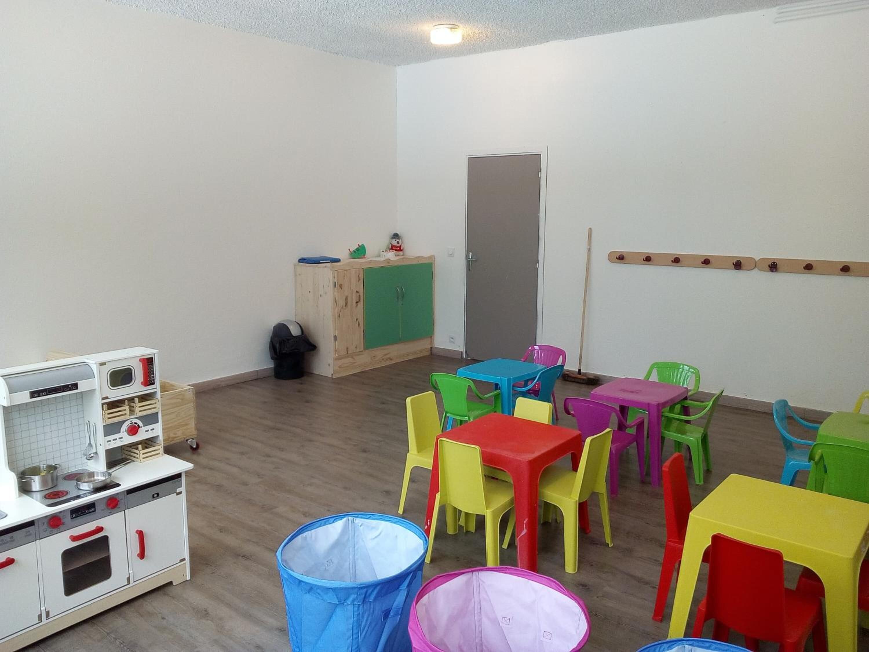 Una sala de juegos infantil con una cocina de juguete, sillas coloridas y mesas.
