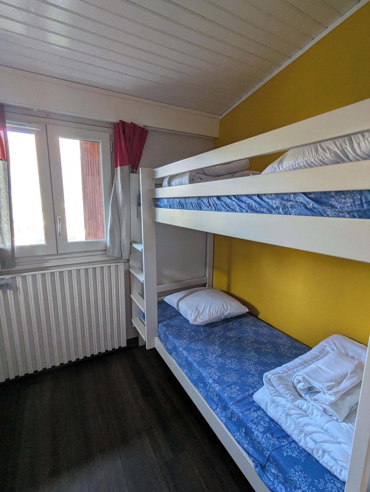 Dormitorio con literas, ventana, radiador y cortinas.