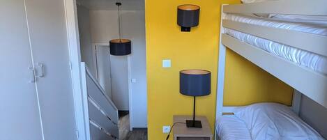 Una habitación con una cama individual superpuesta, un escritorio con lámpara y una escalera que lleva a otra habitación.