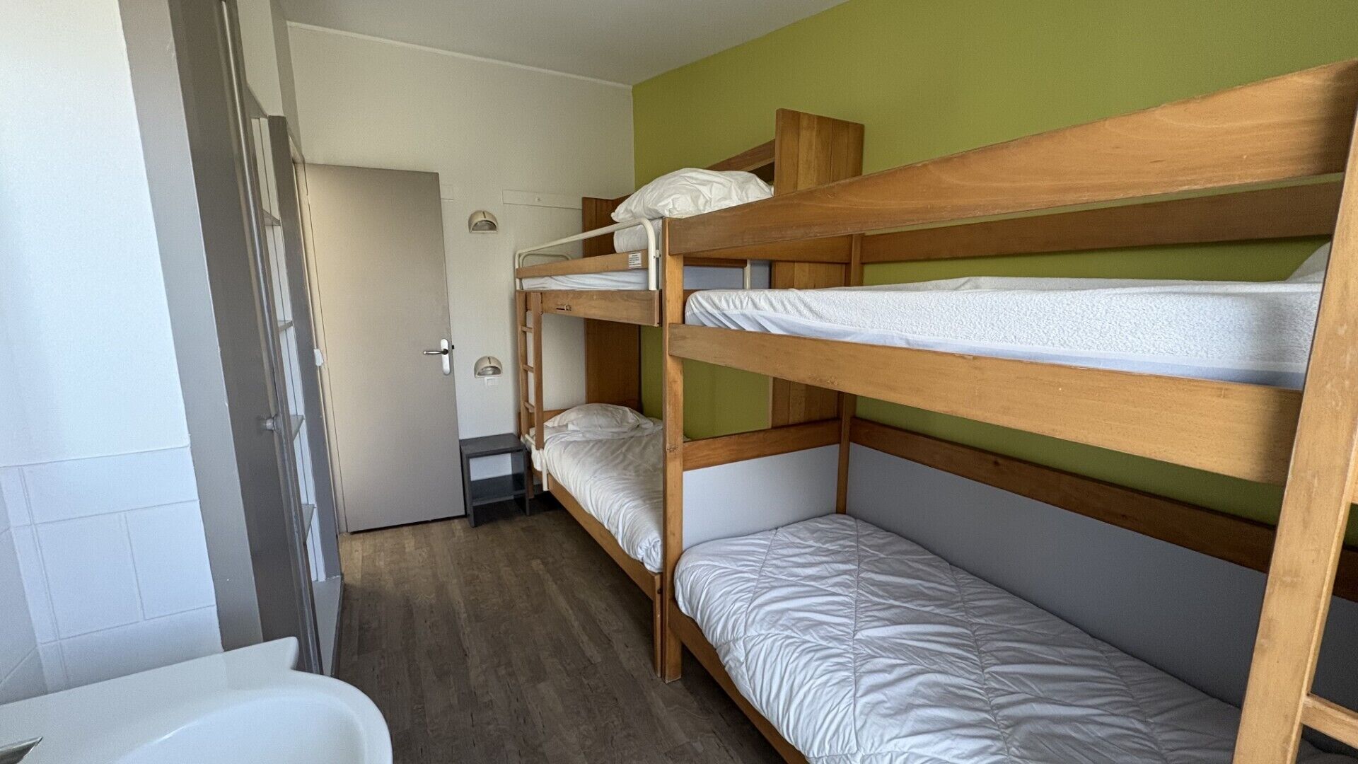 Habitación con literas de madera, una mesita y una puerta.