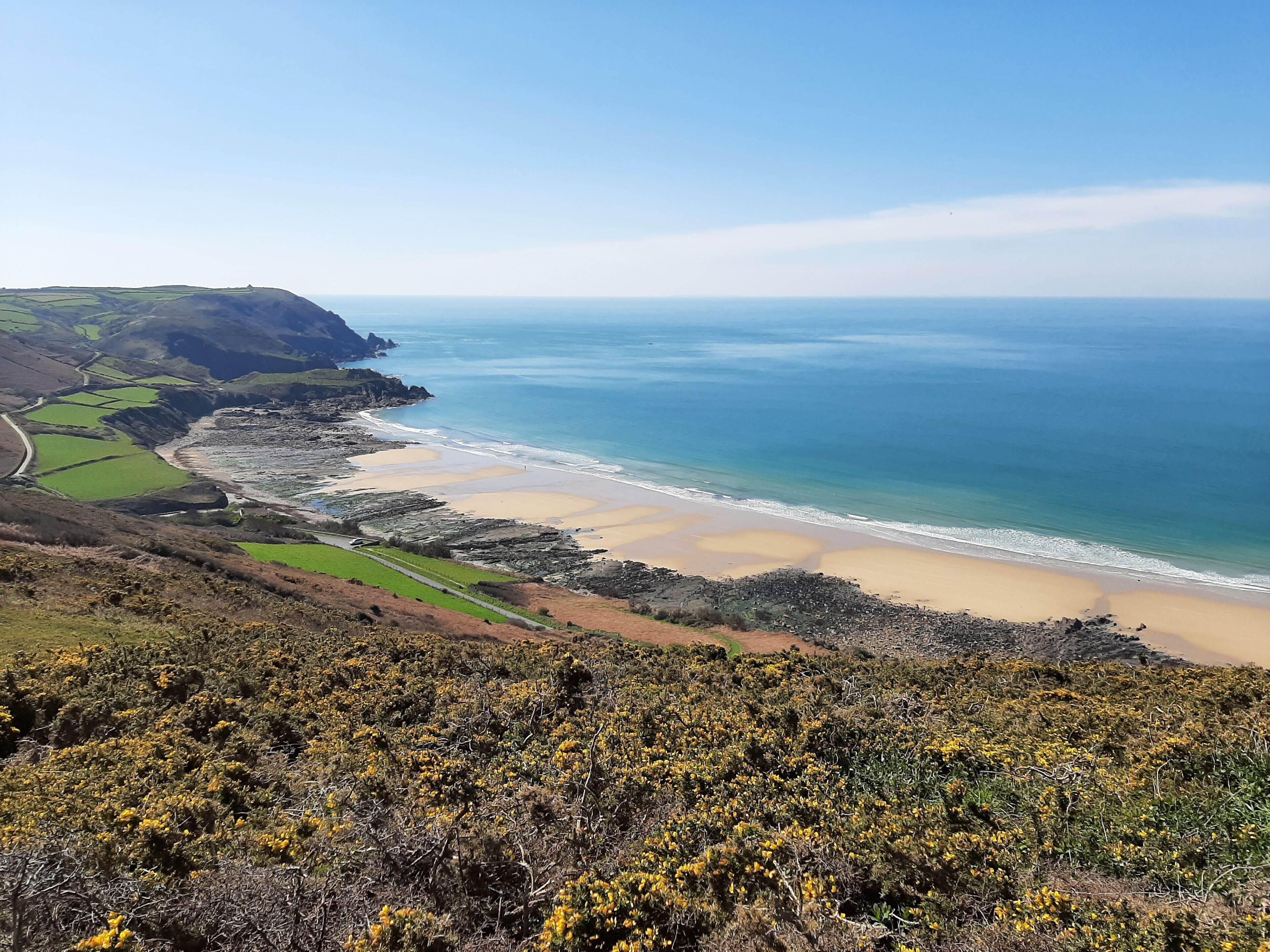 Un paisaje costero con playa, campos verdes y terreno rocoso.