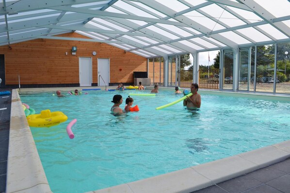 Una piscina interior con paredes de vidrio transparente, paredes de madera y techo cubierto.
