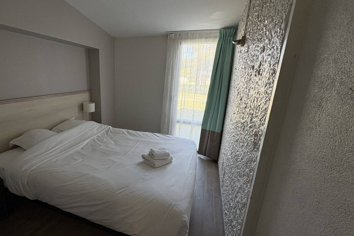 A hotel room with a bed, a nightstand, a lamp, and a window with curtains.