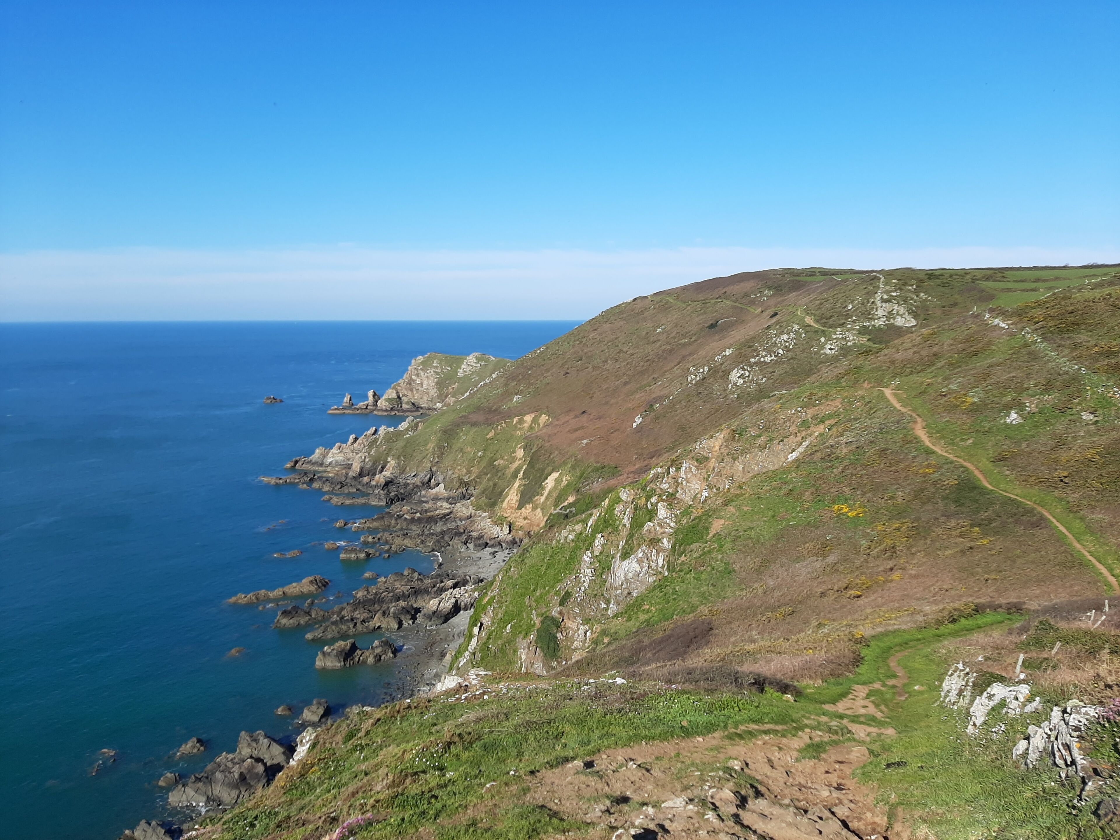 A coastal landscape with rocky cliffs, a clear blue sky, and a winding path along the hillside.