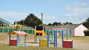 A playground with colorful play structures, a tall chimney, and a building with a red roof in the background.