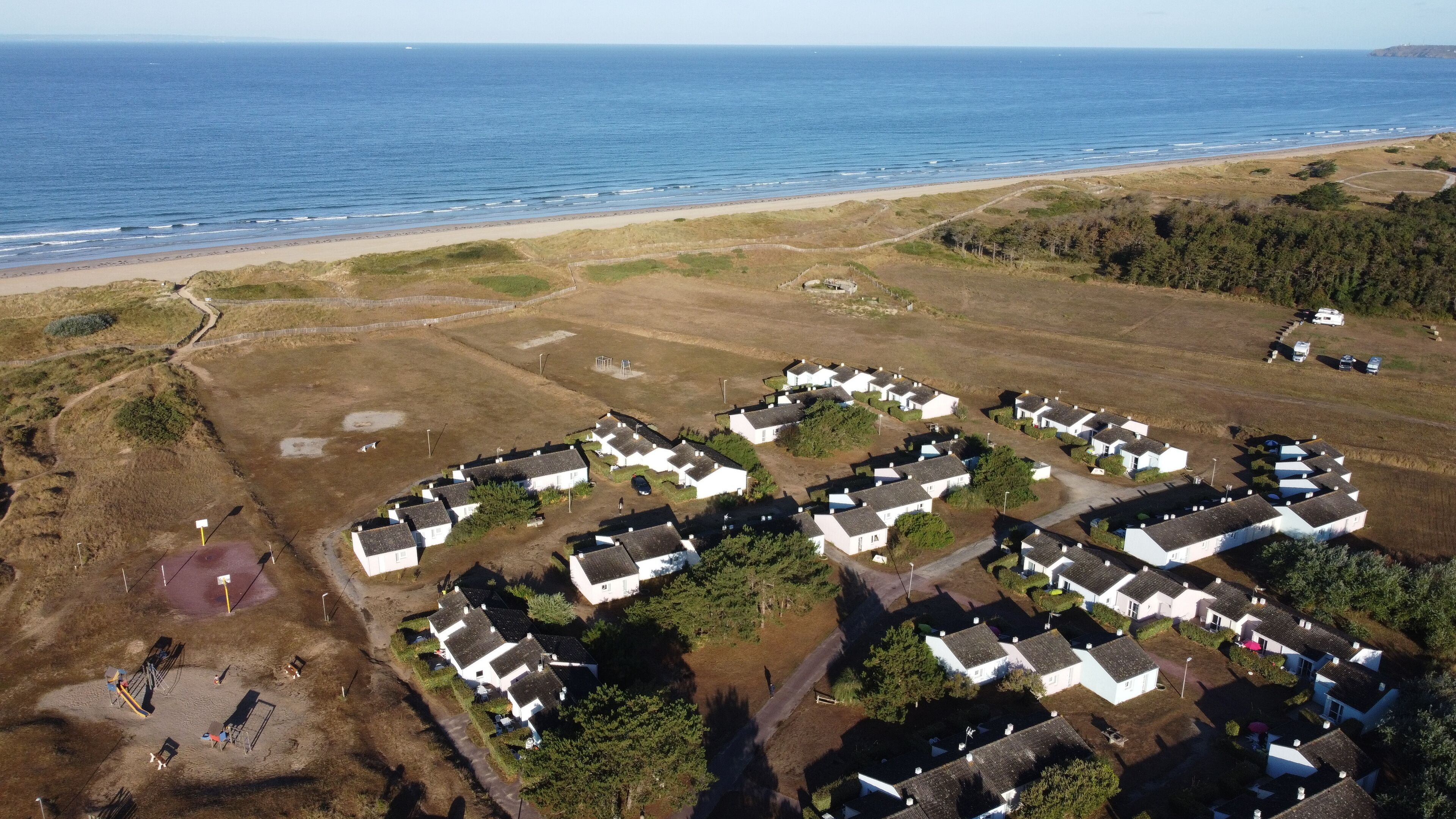 Vue aérienne d’un village côtier avec des maisons blanches, une plage et une vue dégagée sur l’océan.