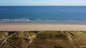 A beach with a sandy shore and grassy dunes in the foreground. - VVF Cotentin Îles anglo-normandes, Port Bail (Port-Bail-sur-Mer)
