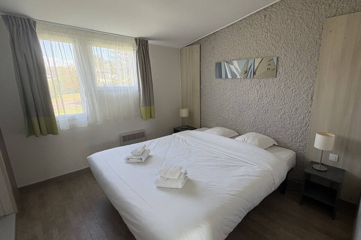 A hotel room with a large bed, two bedside tables, a wall-mounted artwork, and a window with curtains.