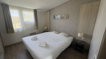 A hotel room with a large bed, two bedside tables, a wall-mounted artwork, and a window with curtains.