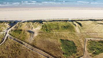 An aerial view of a beach with a sandy shore, grassy dunes, and a wooden boardwalk.