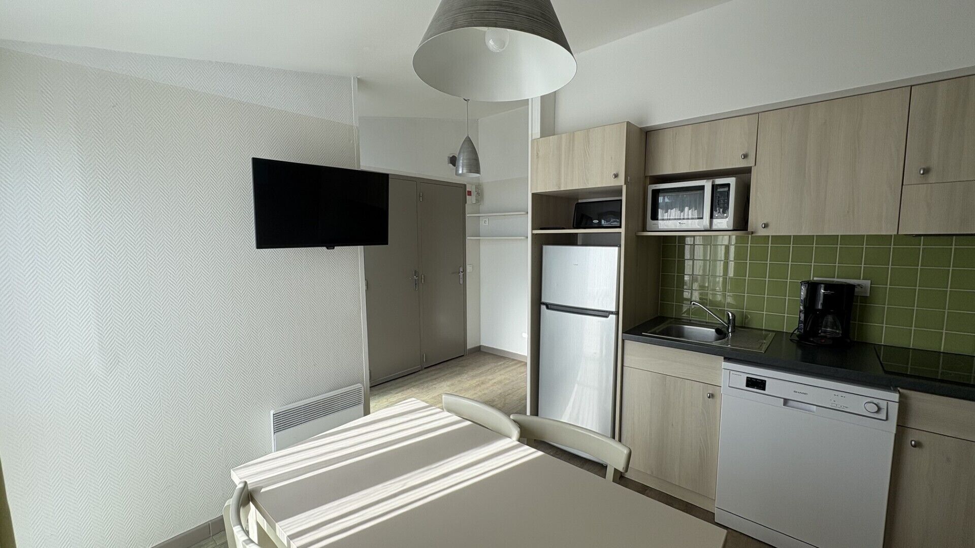 A modern kitchen with a flat-screen TV mounted on the wall, a refrigerator, a microwave, and a coffee maker.