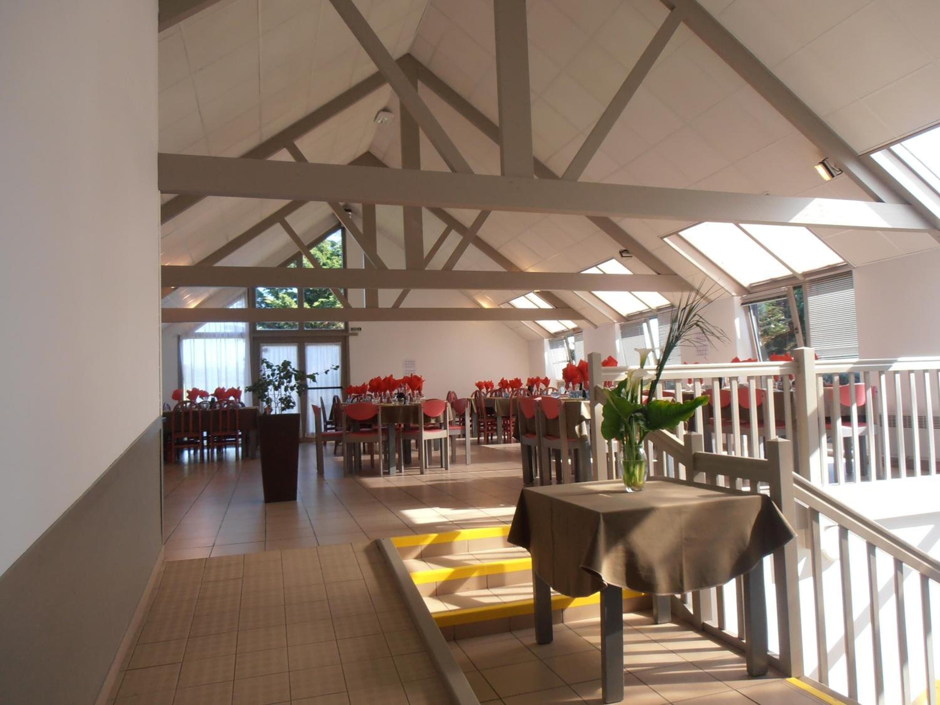 Un vaste espace dédié à la salle à manger, doté de hauts plafonds et de fenêtres de toit, avec des tables dressées et des chaises disposées autour.