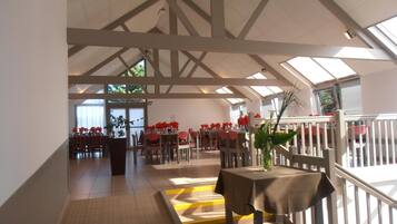 Un vaste espace dédié à la salle à manger, doté de hauts plafonds et de fenêtres de toit, avec des tables dressées et des chaises disposées autour.