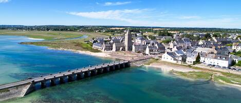 A coastal town with a prominent stone bridge over a clear blue river, surrounded by residential buildings and a historic tower.