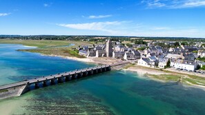 A coastal town with a prominent stone bridge over a clear blue river, surrounded by residential buildings and a historic tower. - VVF Cotentin Îles anglo-normandes, Port Bail (Port-Bail-sur-Mer)