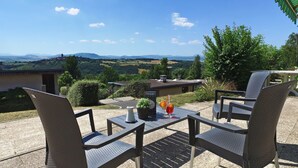 Une terrasse extérieure avec des chaises et une table en osier, une plante en pot et une boisson posée sur la table.
