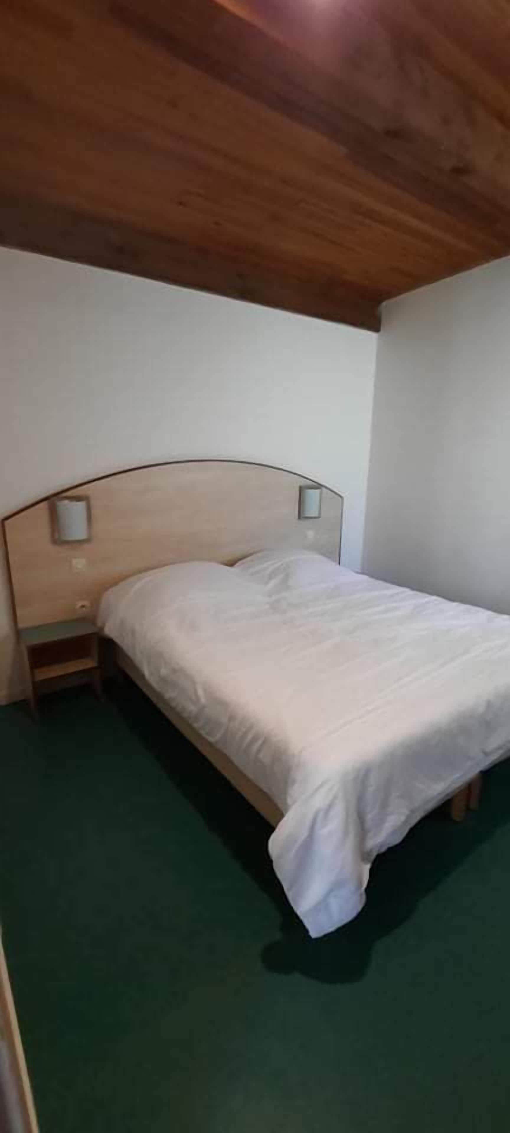 Una cama individual con cabecera de madera y dos mesitas de noche en una habitación con alfombra verde y paredes blancas.