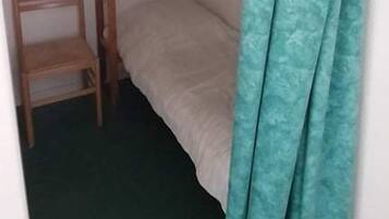 Una habitación pequeña y funcional con una cama litera, una silla de madera y una cortina color turquesa.