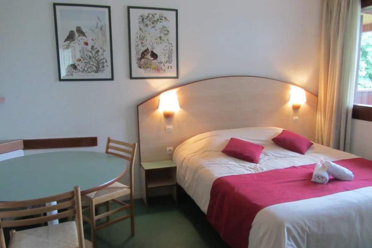 Une chambre d’hôtel avec un lit, une table et des chaises, et deux lampes fixées au mur.