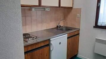 Una cucina compatta con mobili in legno, un piccolo frigorifero e una finestra con tende.