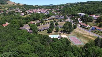 An aerial view of a residential area with houses, a tennis court, and surrounding greenery.