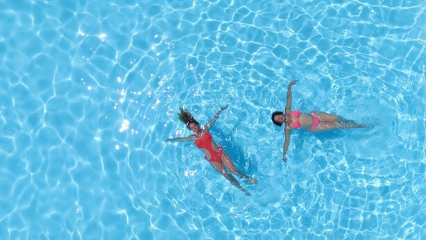 Deux personnes nagent dans une piscine à l’eau claire et bleue.