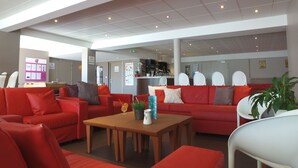 Un hall d’entrée spacieux avec des canapés rouges et une table basse en bois, un espace d’accueil doté d’un comptoir et de chaises, et un bar situé au fond de la pièce.