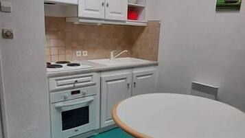 Une cuisine de taille réduite avec des meubles blancs, une cuisinière et une table ronde.