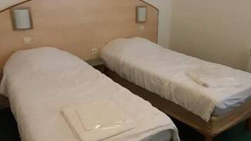 A room with two single beds, wooden headboards, and a green carpet.