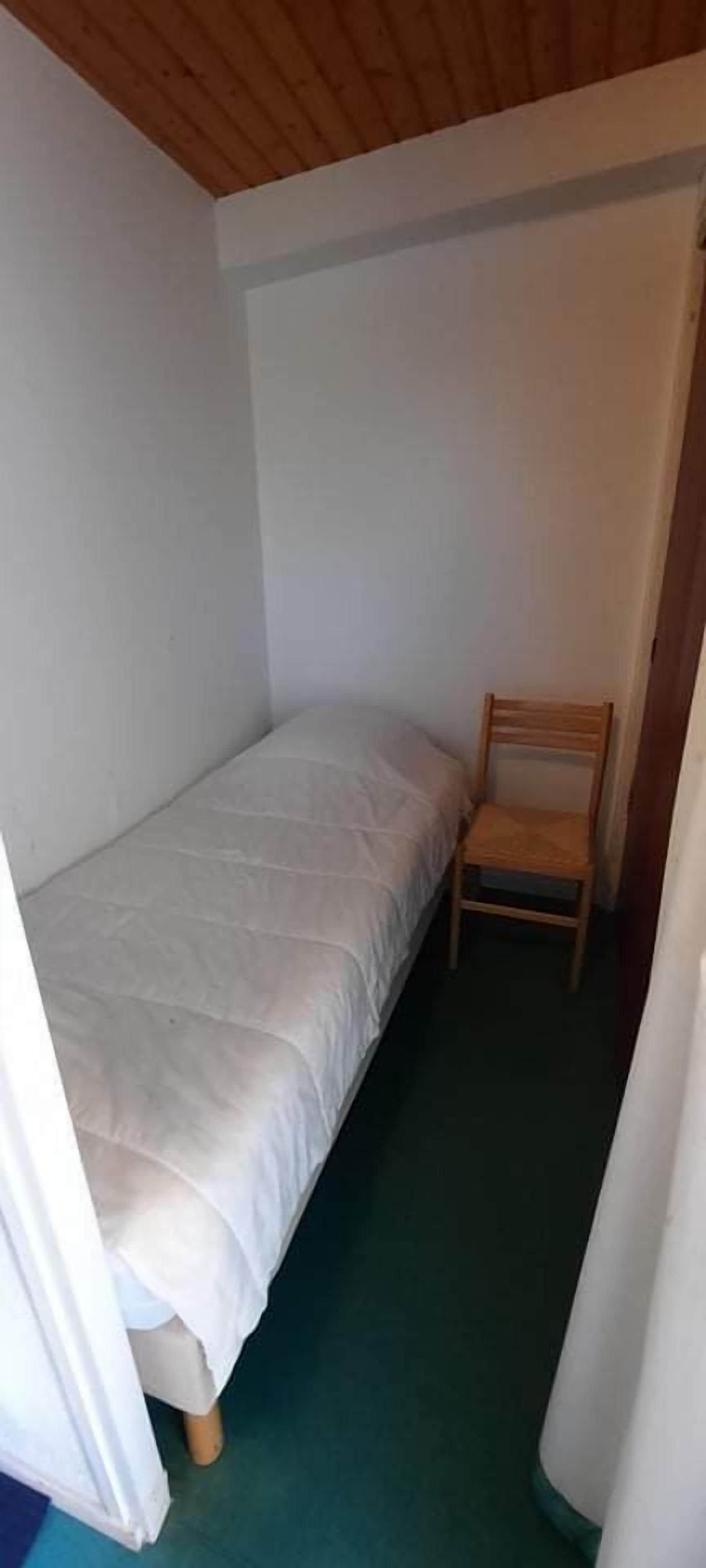 Una habitación pequeña con una cama individual, una silla de madera y una alfombra verde.