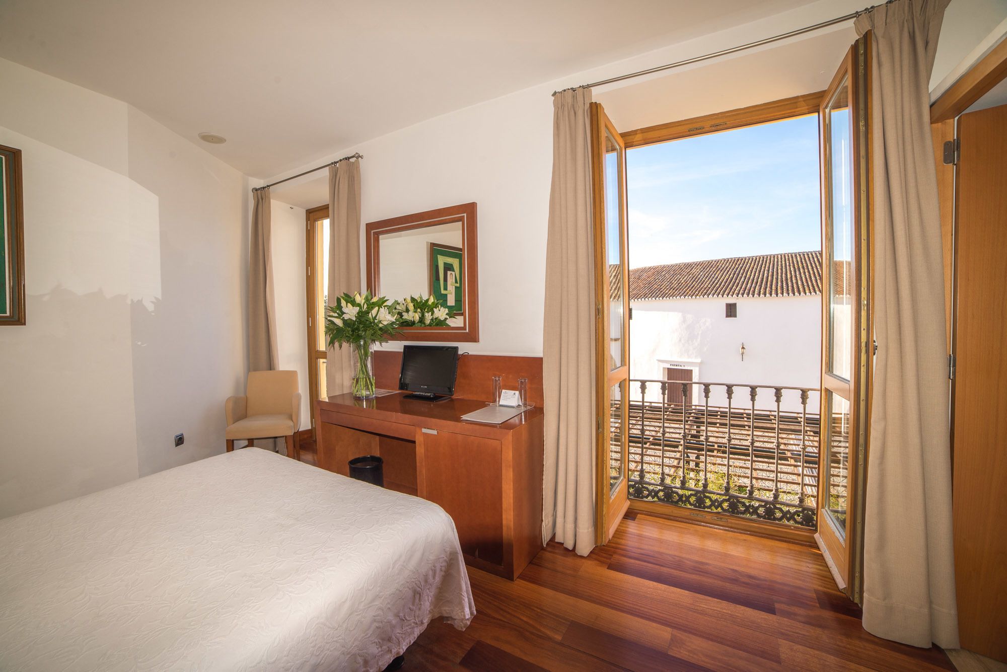A hotel room with a bed, a desk with a computer, a mirror, and a view of a courtyard.